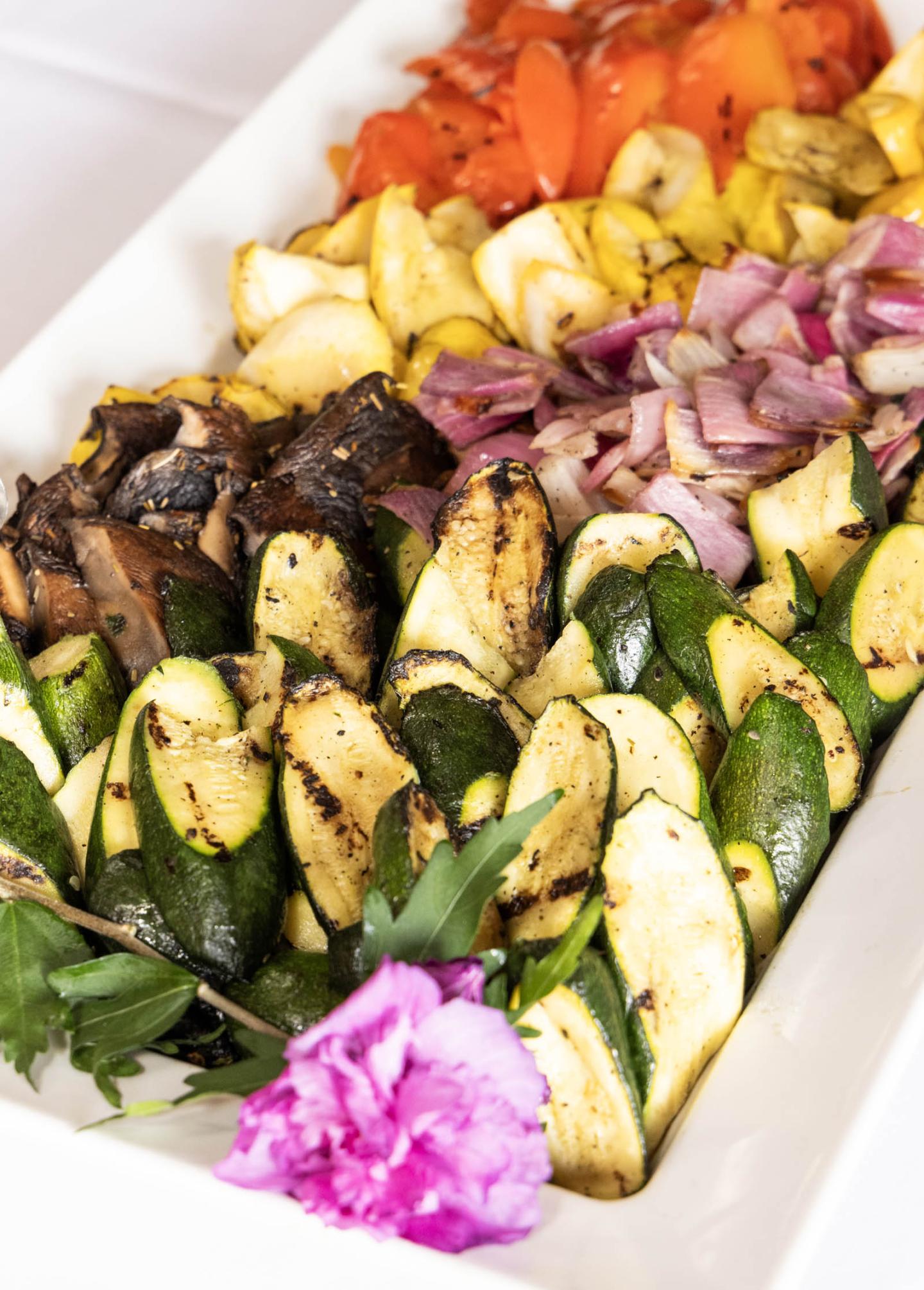 Grilled vegetables on a platter with a pink flower garnish.